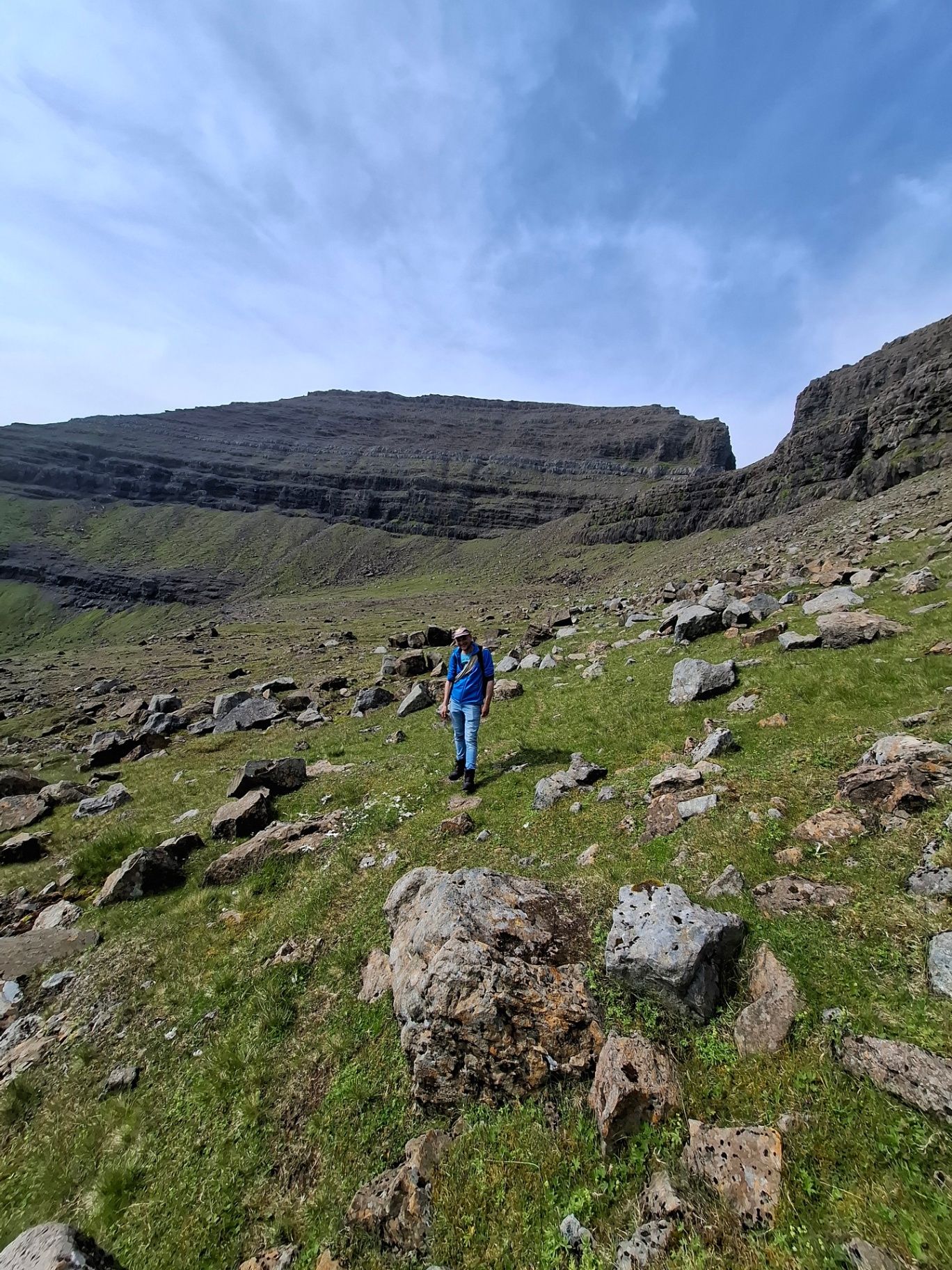 A single walker crossing a boulder field beneath basalt cliffs