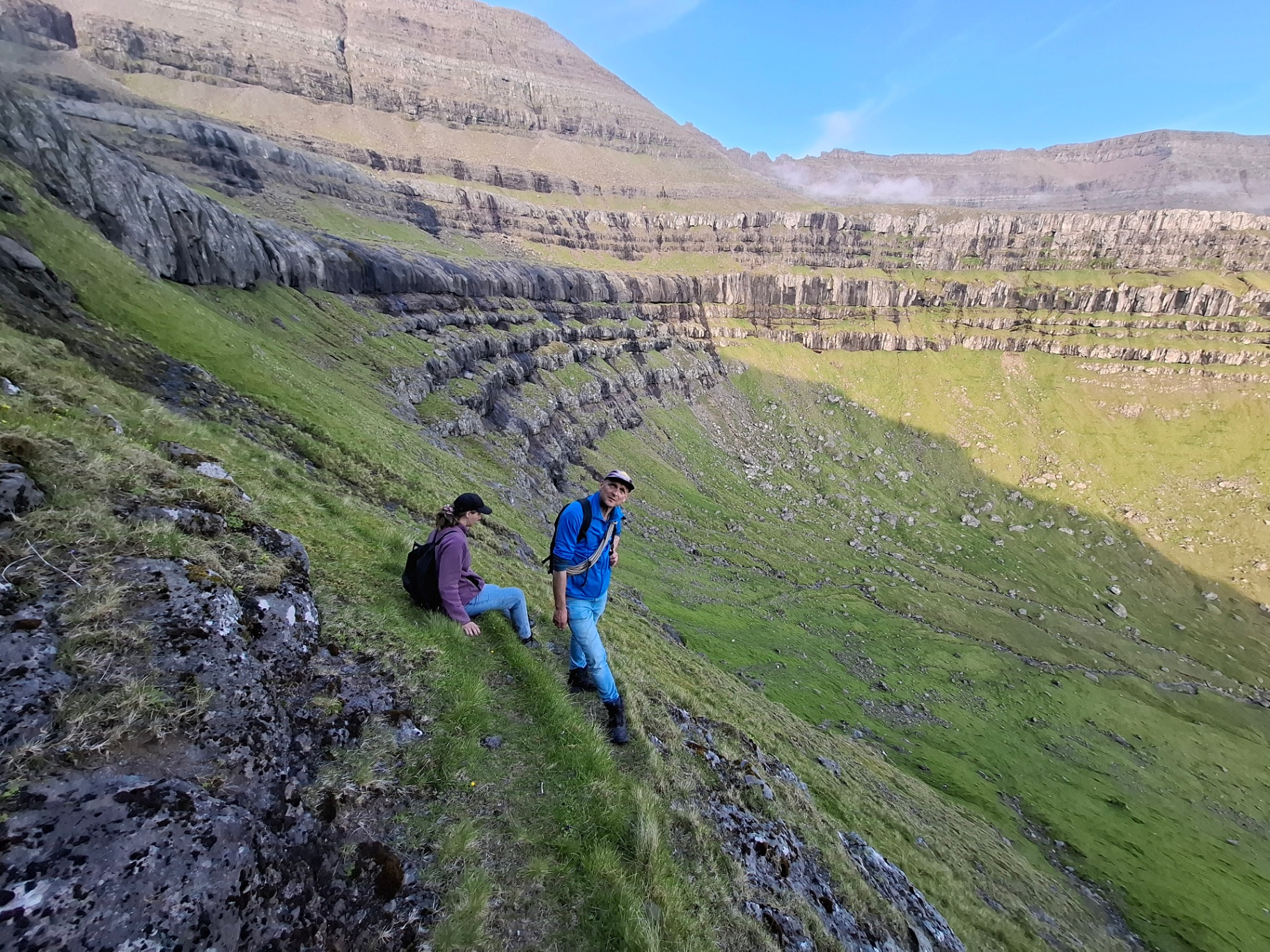 A host and a hiker resting on a steep green mountainside