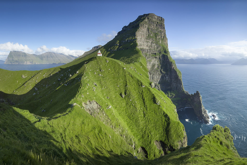 The Kallur lighthouse on a green ridge above Atlantic sea cliffs
